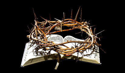 The crown of thorns lies on the open book of the Bible. Objects on an isolated black background.