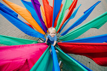 Picture of little caucasian boy in blue summer clothes is surrounded by colourful flags outside