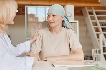 Warm-toned portrait of mature bald woman talking to female doctor comforting and congratulating her...