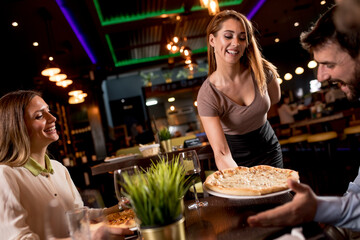 Waiter woman serving group of friends with food in the restaurant