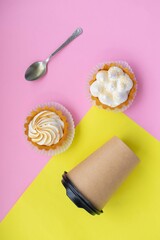 Top view of sweet cakes, white cream next to a cup of coffee and a spoon on a pink and yellow background. There space for text and mock up