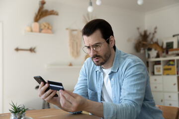 Distressed young Caucasian man make online payment or purchase on smartphone have problems with...