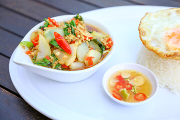 Pad Ka-prao; stir fried chopped chicken with chili and basil, served with steamed rice and fried egg on top set on wooden table