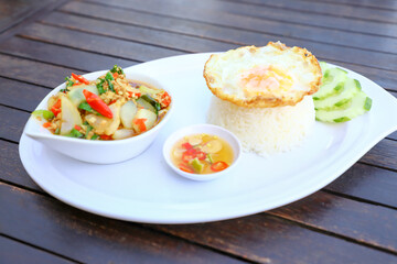Pad Ka-prao; stir fried chopped chicken with chili and basil, served with steamed rice and fried egg on top set on wooden table