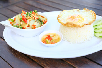 Pad Ka-prao; stir fried chopped chicken with chili and basil, served with steamed rice and fried egg on top set on wooden table