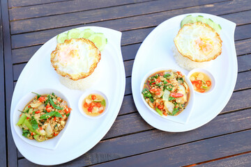 Pad Ka-prao; stir fried chopped chicken with chili and basil, served with steamed rice and fried egg on top set on wooden table