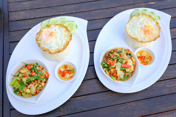 Pad Ka-prao; stir fried chopped chicken with chili and basil, served with steamed rice and fried egg on top set on wooden table