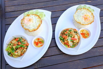 Pad Ka-prao; stir fried chopped chicken with chili and basil, served with steamed rice and fried egg on top set on wooden table
