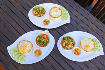 Pad Ka-prao; stir fried chopped chicken with chili and basil, served with steamed rice and fried egg on top set on wooden table