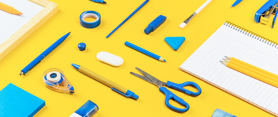 Assorted office and school white and blue stationery on bright yellow background. Organized...