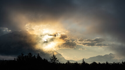 Morgenlicht bricht zwischen Wolken und hinter einem Berg hervor