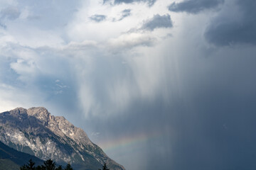 Regenbogen bildet sich unter einem Schauer an einer Bergflanke