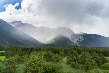 Regenschauer in einem Hochtal zwischen Bergwald und Felswänden