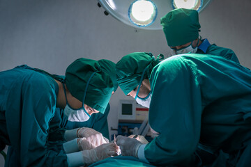 Medical team in uniform wearing face mask and gloves doing surgery with medical tools in operation room at hospital.