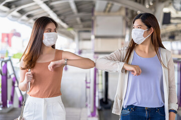 Young Asian woman passenger wearing surgical mask and elbows bump with friend together in subway...