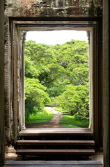 One of the dozens of entrances of the Angkor wat temple with the jungle thet can be seen through the doorway.