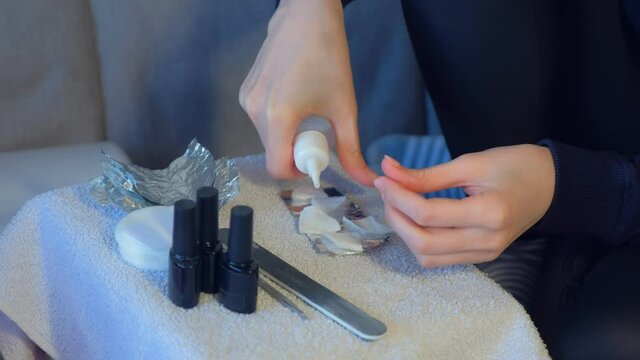 Woman pouring remover to cotton pads to remove shellac from nails, hands closeup. Making manicure at home by herself. She prapering foil to nails.