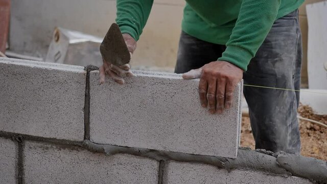close up at the bricklayer  hands, the builder puts the bricks at construction site