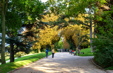 People enjoying tree-lined alley-ways of the Buttes-Chaumont park in Paris, France
