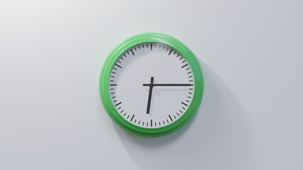 Glossy green clock on a white wall at quarter past six. Time is 06:15 or 18:15