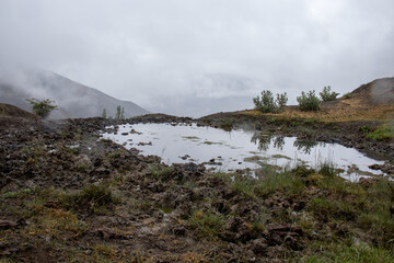 A beautiful mountain lake against with heavy foggy. A small lake in the mountains against the background of fog. A puddle of rain in the mountains. Mountains in the fog