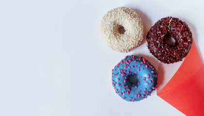 Sweet delicious doughnuts in chocolate, blue and white glazes fall out of a red bag on a light background. Free space for copying. Donuts as a delicious snack, sweet pastry dessert