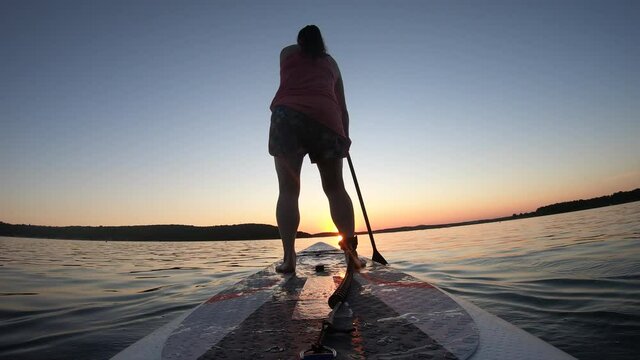 LD Low angle shot of a woman riding a SUP towards the sunset