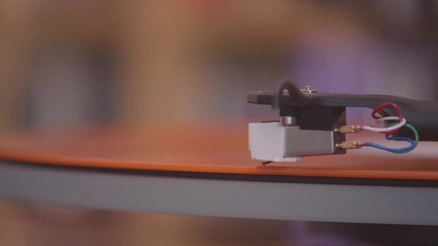 Spinning and lowering stylus onto an orange vinyl lp extreme close up