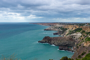 beautiful seascape of Cape Fiolent, Crimea. Calm azure sea and rocky coast. Sky with blue clouds. City by the sea.