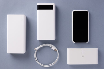 three various Power bank chargers of different capacities, USB cable and smartphone on a blue background. Modern digital concept. top view.