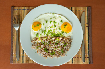 Breakfast with fried eggs and buckwheat porridge on a white plate.