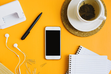 Horizontal flat lay with a smartphone, green tea and school stationery on yellow background. Back to school concept