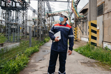 An electrical substation engineer inspects modern high-voltage equipment in a mask at the time of...