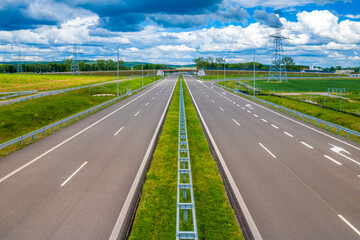 Straight asphalt highway passing through the rural area in the mountains at sun and clouds spring weather. Concept of travel, quick trip, transport, fast moving forward ideas or road construction