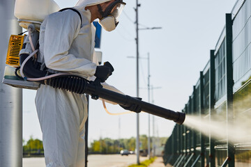 side view on professional disinfector man in suit applying powerful disinfectant spray on contaminated area