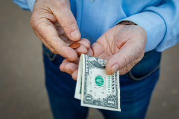 Hands of an elderly man with one us dollar and one cent, the elderly man counts his money. The concept of poverty, small pension, lack of savings.