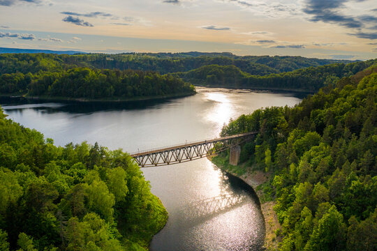 Aerial view of steel underspanned suspension railway bridge over Bobr River in Pilchowice, beautiful lake with islands and green forests in mountains on a sunny summer day in Pilchowice, Poland