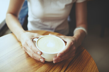Fototapeta na wymiar Female hands holding cup of coffee in cafe. Blurred image, selective focus
