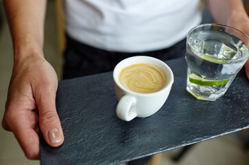 Female hands holding stone plate with cup of coffee and water in a glass with lime.Coffee break.Blurred image,selective focus