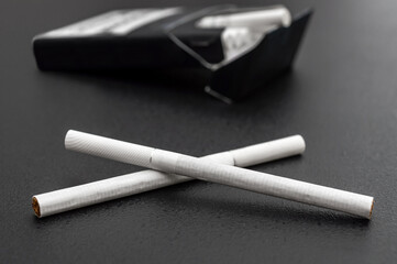 Thin cigarettes with cigarette pack on black. Close up.