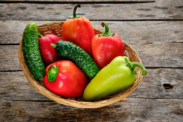 Sweet bell peppers and cucumbers in a wicker basket on a rustic wooden table.