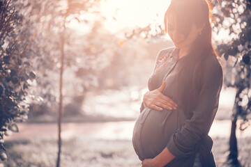 Pregnant happy Woman touching her belly. Full length Pregnant beauty young mother outdoor portrait, caressing her belly and smiling. Healthy Pregnancy concept, brunette expectant female in summer park