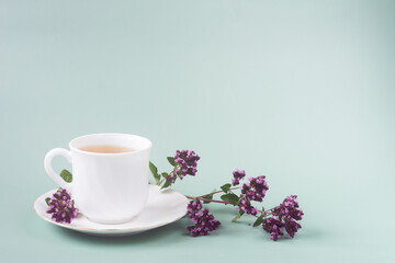 Obraz na płótnie Canvas a white Cup of tea with a sprig of oregano stands on the table on a gray-green background, morning tea
