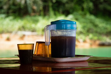 Ice coffee in a plastic container with empty glasses next to it. Traditional cold summer drink in an outdoor in Malaysia.