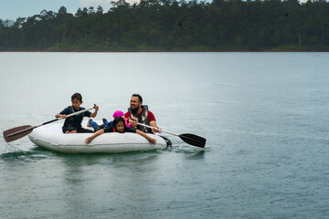 Family wearing life jackets paddling on an inflatable boat in Kenyir Lake, Malaysia.