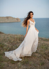Fototapeta na wymiar Tender and beautiful bride closed her eyes and dreams standing in the autumn meadow after sunset with a view of the Bay and promontory.