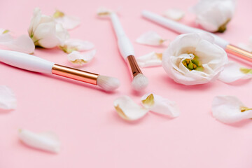 Fototapeta na wymiar Makeup brushes and flowerss on white background. Top Horizontal view copyspace.