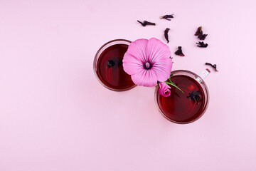 Hot tea from hibiscus or sudanese rose in glass mugs with pink flower and dry tea leaves on pink background. Top view. Copy space.  