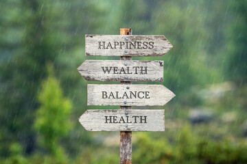 happiness wealth balance health text on wooden signpost outdoors in the rain.