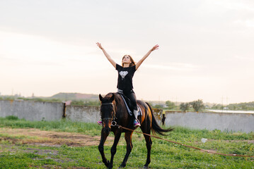A young and pretty girl is learning to ride a thoroughbred Mare on a summer day at the ranch. Horse...